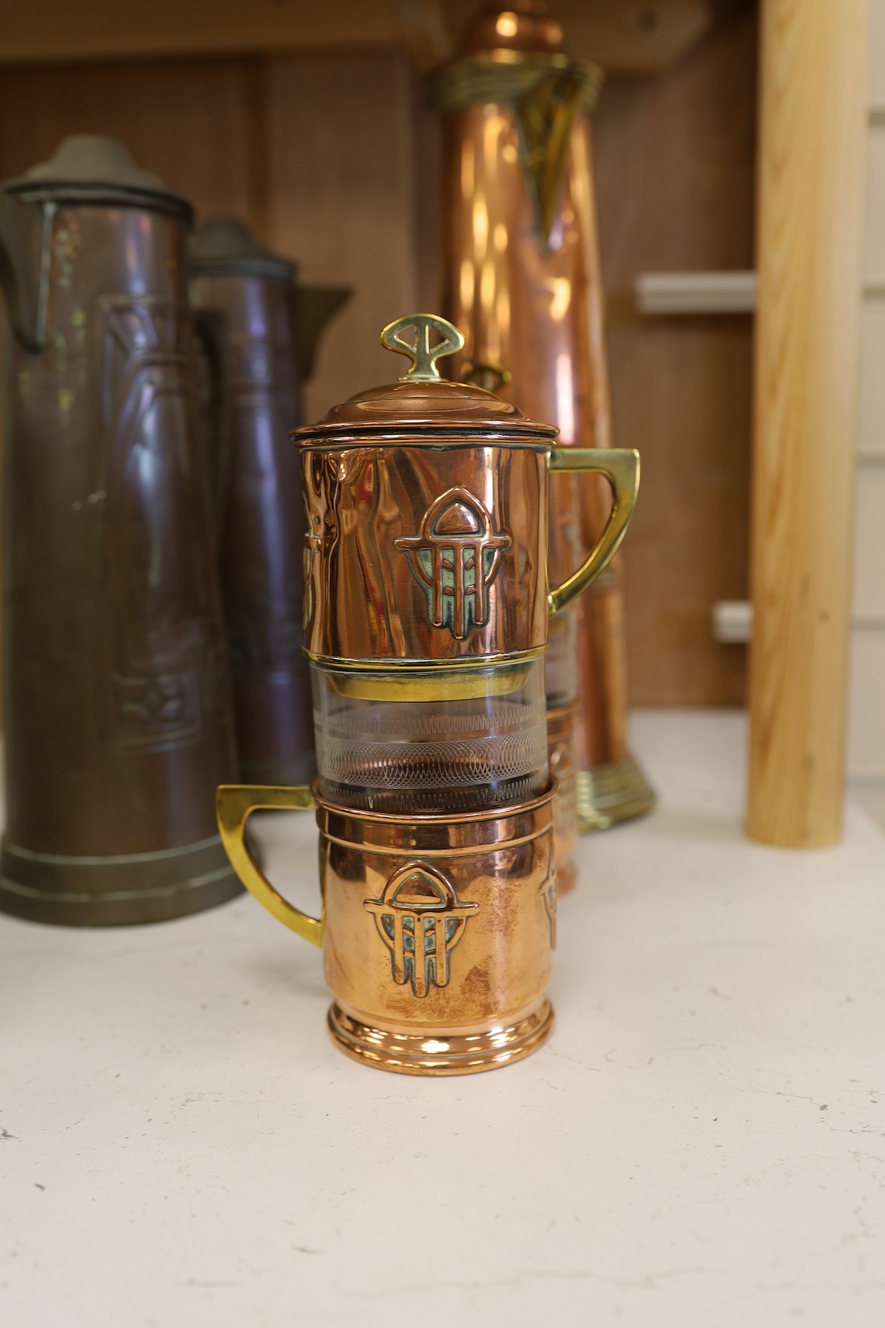 Three Art Nouveau mixed copper and brass coffee pots and two individual copper filter coffee glasses, tallest 36cm high (5). Condition - two pots need cleaning, but good condition for age